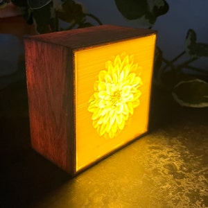 May include: A wooden box with a light-up image of a white flower. The flower is in the center of the box and is illuminated from behind, creating a soft glow.
