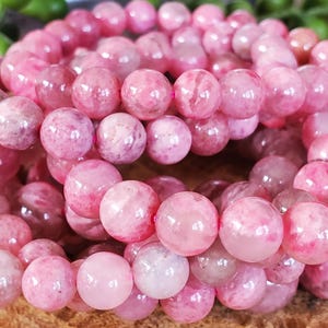 May include: Close-up of a bracelet made of pink gemstone beads. The beads are round and vary in shades of pink, from light to deep rose. The bracelet is strung on a pink elastic cord, creating a continuous loop.