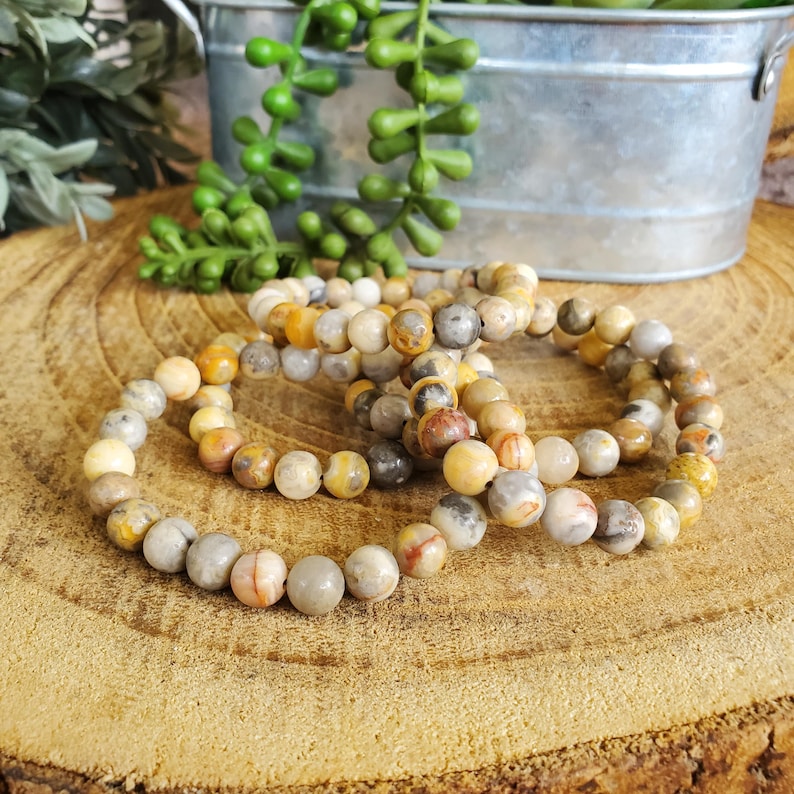 Pode incluir: Quatro pulseiras feitas com contas de &aacute;gata marrom, branco e amarelo. As pulseiras est&atilde;o empilhadas umas sobre as outras em uma superf&iacute;cie de madeira.