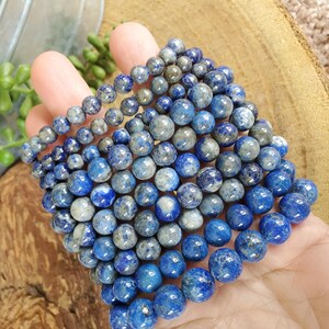 May include: Several strands of blue lapis lazuli gemstone beads in varying sizes. The beads have a mix of deep blue and gray tones, with a polished, round shape. The beads are held in a hand.