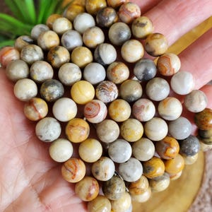 Pode incluir: Um close-up de um fio de contas redondas de &aacute;gata amarela, marrom e branca. As contas s&atilde;o de tamanhos diferentes e t&ecirc;m um acabamento natural e polido.