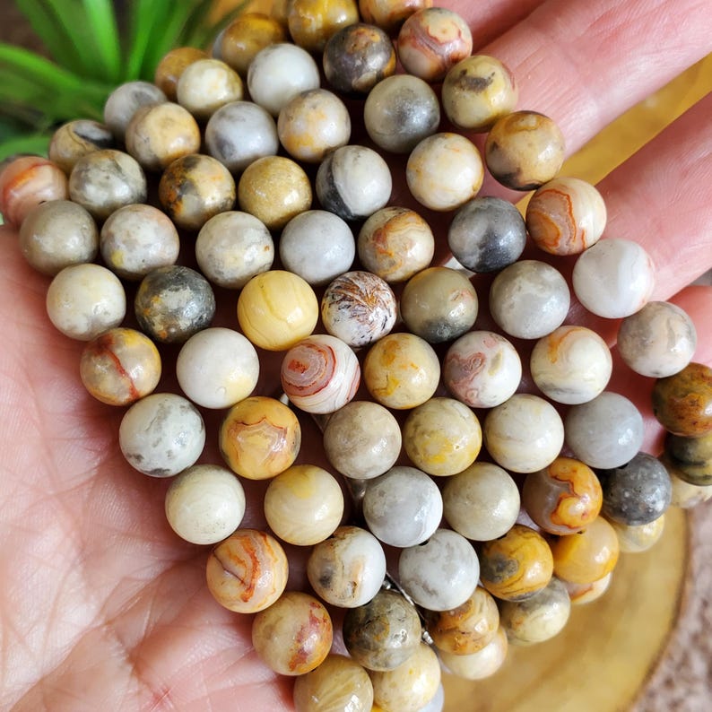 Pode incluir: Um close-up de um fio de contas redondas de &aacute;gata amarela, marrom e branca. As contas s&atilde;o de tamanhos diferentes e t&ecirc;m um acabamento natural e polido.