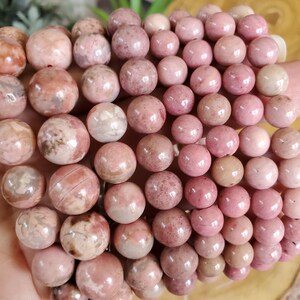 May include: A close-up of a pile of pink and white gemstone beads. The beads are round and have a smooth, polished finish. They are arranged in a random pattern, creating a visually appealing display.