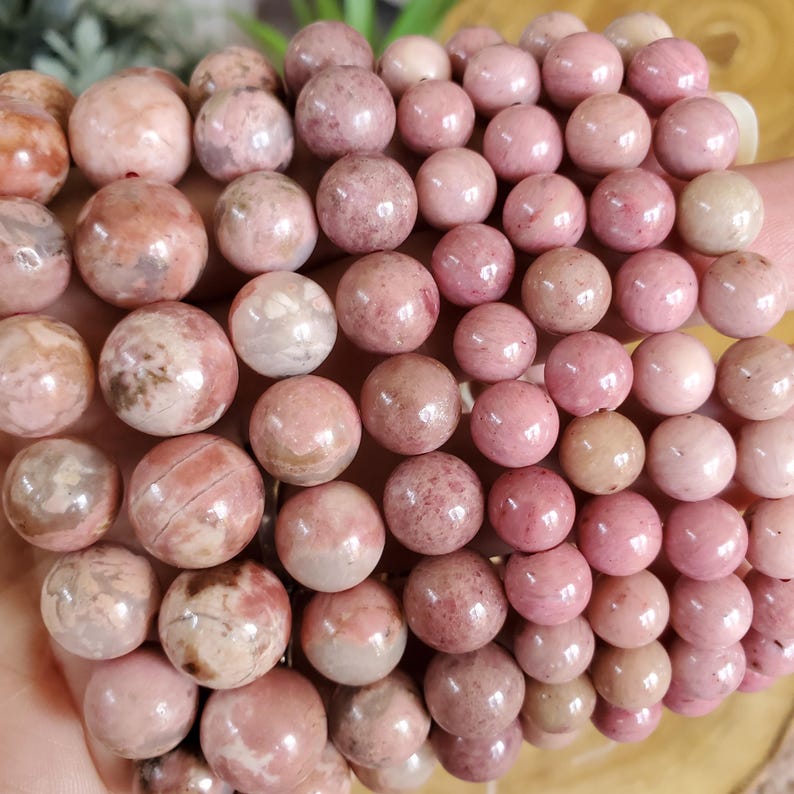May include: A close-up of a pile of pink and white gemstone beads. The beads are round and have a smooth, polished finish. They are arranged in a random pattern, creating a visually appealing display.