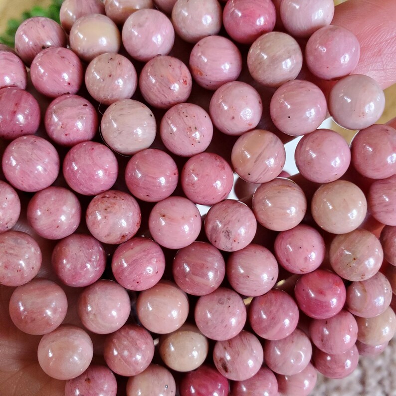 May include: A close-up of a pile of pink and white round beads. The beads are smooth and have a natural, polished look.