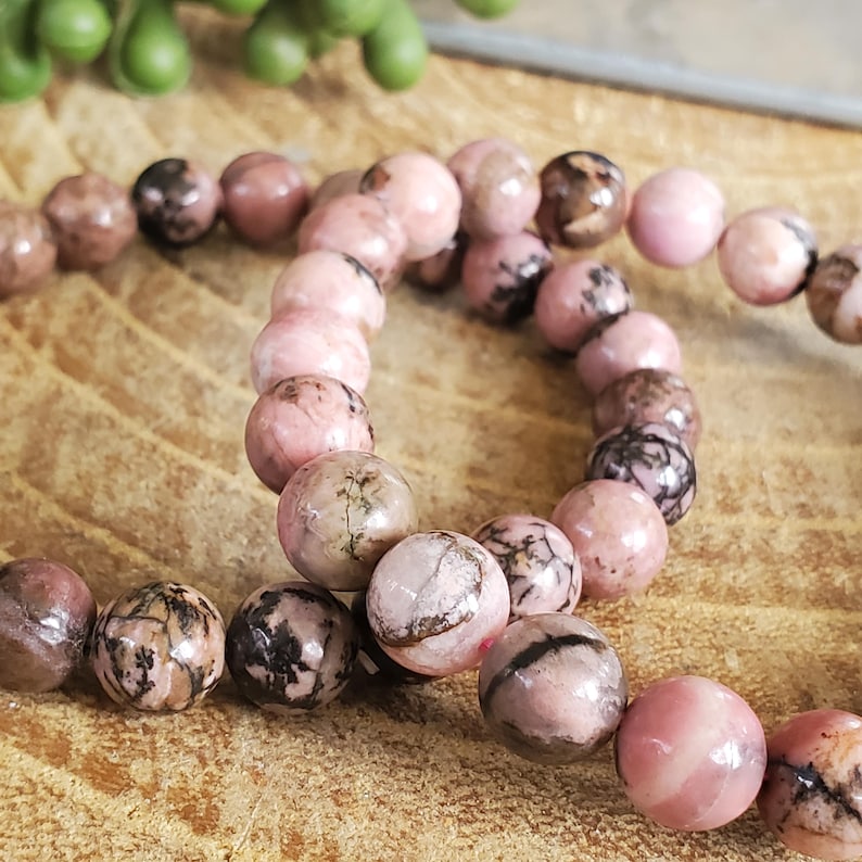 Puede incluir: Dos pulseras de piedras preciosas rosas y negras con cuentas redondas.