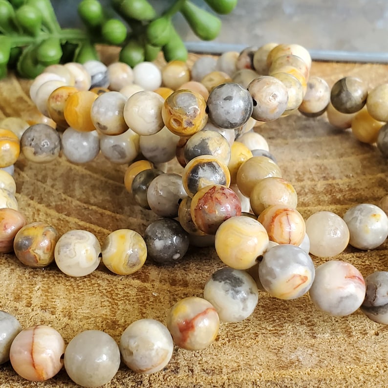 Pode incluir: Um conjunto de pulseiras feitas com contas de &aacute;gata amarela, marrom e cinza. As contas s&atilde;o redondas e t&ecirc;m um acabamento natural e polido.