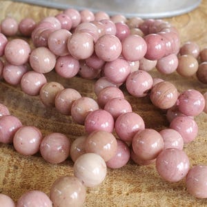 May include: A close-up of a pile of pink and white gemstone beads. The beads are round and smooth, and they have a natural, polished finish.