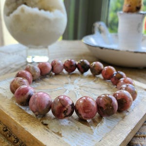 Puede incluir: Un brazalete de piedras preciosas rosa y marr&oacute;n con cuentas redondas. El brazalete est&aacute; hecho de piedras naturales y tiene un patr&oacute;n &uacute;nico de m&aacute;rmol.