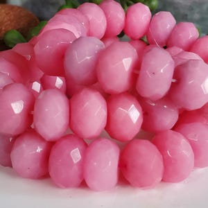 May include: Close-up of a strand of faceted, light pink beads. The beads are oval-shaped with multiple facets, creating a sparkling effect. The beads are strung together, suggesting they are for jewelry making.