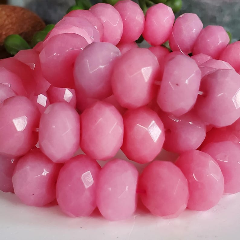 May include: Close-up of a strand of faceted, light pink beads. The beads are oval-shaped with multiple facets, creating a sparkling effect. The beads are strung together, suggesting they are for jewelry making.