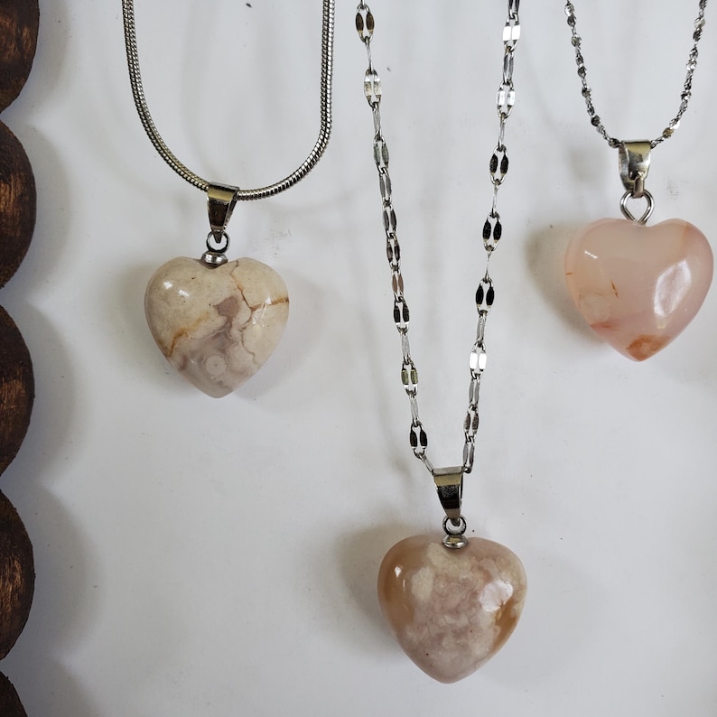 Op de afbeelding: Drie kettingen met hartvormige hangers. De hangers zijn gemaakt van steen in beige en roze tinten. De kettingen zijn zilverkleurig en vari&euml;ren in stijl. De kettingen worden gepresenteerd tegen een witte achtergrond.