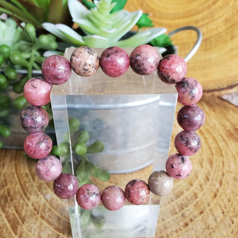 Puede incluir: Un brazalete de piedras preciosas rosa y negro con cuentas redondas. El brazalete est&aacute; hecho de piedras naturales y tiene aproximadamente 18 cm de largo.