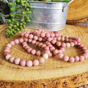 May include: A set of pink gemstone bracelets made with round beads. The bracelets are stacked on top of each other on a wooden surface.