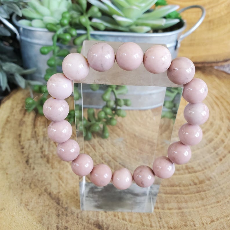 Puede incluir: Un brazalete de piedras preciosas rosas con cuentas redondas. El brazalete est&aacute; en un expositor transparente.