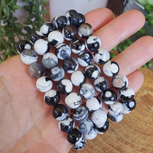 May include: A collection of round beads in shades of black, white, and gray. The beads have a marbled appearance, with swirling patterns and variations in color. The beads are smooth and polished, and appear to be made of stone or a similar material.