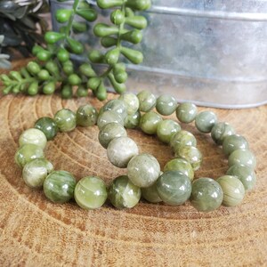 May include: Two green gemstone bracelets with round beads. The bracelets are made of a light green stone with darker green streaks.