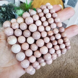 Puede incluir: Una pila de pulseras de piedras preciosas rosas y blancas. Las pulseras est&aacute;n hechas de cuentas redondas con un acabado liso y pulido.