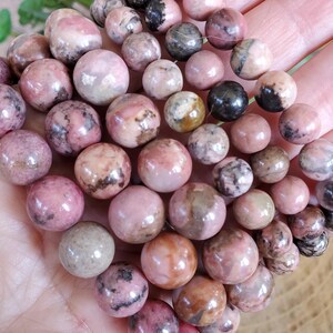 Puede incluir: Primer plano de un mont&oacute;n de cuentas redondas de piedra preciosa rosa y blanca. Las cuentas son lisas y tienen un acabado natural y pulido.