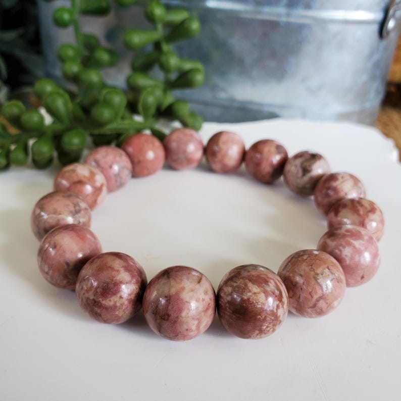 May include: A pink and brown stone bracelet with round beads. The bracelet is made of natural stone and has a unique marbled pattern.