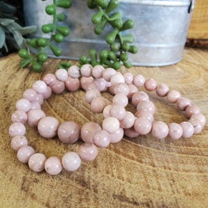 Puede incluir: Tres pulseras de piedras preciosas rosas con cuentas redondas. Las pulseras est&aacute;n apiladas una encima de la otra.