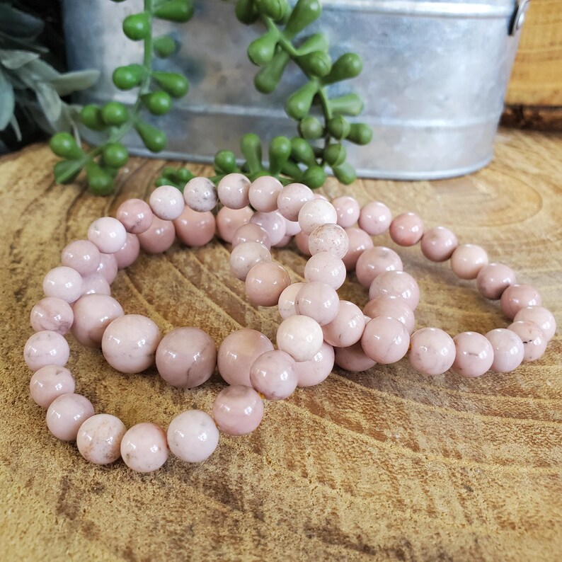 Puede incluir: Tres pulseras de piedras preciosas rosas con cuentas redondas. Las pulseras est&aacute;n apiladas una encima de la otra.