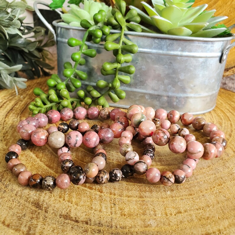 Puede incluir: Un conjunto de cuatro pulseras de piedras preciosas rosas y marrones. Las pulseras est&aacute;n hechas de cuentas redondas y est&aacute;n apiladas unas sobre otras.
