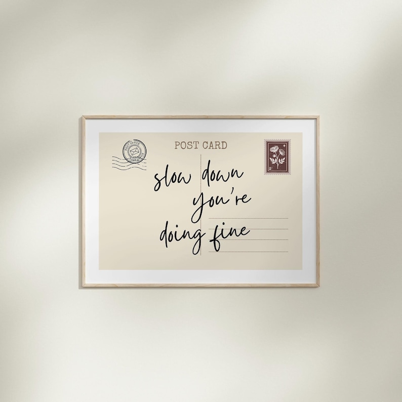 May include: A framed postcard print with the words "slow down you're doing fine" in black script. The postcard has a vintage aesthetic with a postage stamp and postmark design.