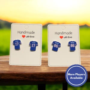 May include: Two pairs of handmade football jersey earrings. The earrings are blue with white lettering and numbers. The left pair features the number 17 with the name "ALLEN" above it. The right pair features the number 86 with the name "KINCAID" above it. The earrings are displayed on white cards with the text "Handmade with love".