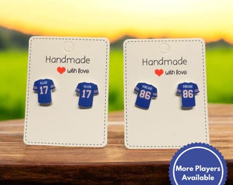 Puede incluir: Dos pares de pendientes hechos a mano con forma de camiseta de fútbol. Los pendientes son azules con letras y números blancos. El par izquierdo presenta el número 17 con el nombre "ALLEN" encima. El par derecho presenta el número 86 con el nombre "KINCAID" encima. Los pendientes se muestran en tarjetas blancas con el texto "Handmade with love".