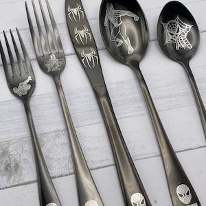 Puede incluir: Conjunto de cinco cubiertos de acero inoxidable negro con diseños de Spiderman. El conjunto incluye un cuchillo, dos tenedores y dos cucharas. Cada pieza tiene un logotipo de Spiderman y un diseño de Spiderman diferente.