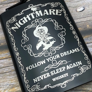 May include: Black metal flask with a silver engraved design featuring a character with a knife and the text "Nightmare, Follow Your Dreams, Never Sleep Again, Whiskey".