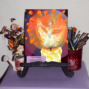 May include: A painting of a woman in a white dress dancing on a candle. The background is a colorful circle with orange petals. The painting is titled "Calor de nostalgia" and has the text "Frágil llama que es la vida, incluso sabiendo lo efimera que es".