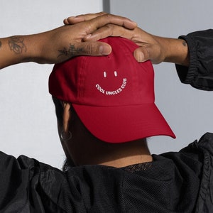 May include: Red baseball cap with white embroidered text that reads "Cool Uncles Club" and a smiley face.