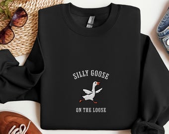May include: Black sweatshirt with white text that reads "Silly Goose on the Loose" and a white embroidered image of a goose running.