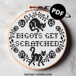 May include: A circular wooden embroidery hoop containing white fabric with a black cross-stitch pattern. The design features two black cats and a floral border surrounding the text BIGOTS GET SCRATCHED. A black circular icon with white PDF text is visible.