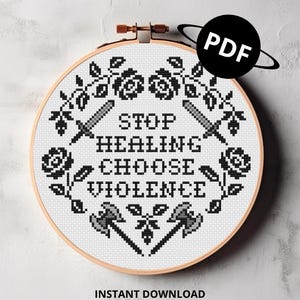 Op de afbeelding: Een kruissteekontwerp in een houten hoepel met de tekst "STOP HEALING CHOOSE VIOLENCE" in zwart. Het ontwerp bevat zwaarden, bijlen en bloemelementen. Een zwarte cirkel met "PDF" staat rechtsboven. De tekst "INSTANT DOWNLOAD" staat onderaan.