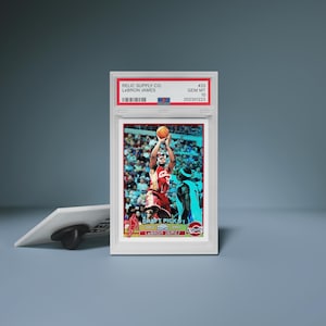 Könnte beinhalten: Eine gerahmte Basketballkarte mit LeBron James in einem rot-weißen Trikot, beim Schuss. Die Karte ist bewertet und in einem weißen Halter mit dem Text "RELIC SUPPLY CO. LEBRON JAMES" und "DRAFT PICK 1" eingeschlossen.