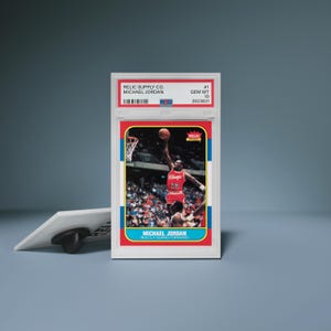 Puede incluir: Una tarjeta de baloncesto de Michael Jordan calificada en una funda protectora blanca. La tarjeta presenta una foto de Jordan con una camiseta roja, en el aire, con el texto "MICHAEL JORDAN" en la parte inferior. La funda tiene el texto "RELIC SUPPLY CO." y "GEM MT 10".