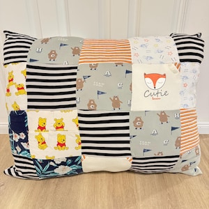 Könnte beinhalten: Ein Patchwork-Kissen mit verschiedenen bunten Stoffen, darunter schwarz-weiße Streifen, orange-weiße Streifen und ein blau-weißer Stoff mit einem Bären-Druck. Das Kissen hat auch einen weißen Stoff mit einem Fuchs-Druck und dem Text "Cutie Bunnies".