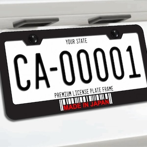May include: A black license plate frame with a white license plate. The license plate reads "CA-00001" in black font. The frame has the text "YOUR STATE" at the top and "PREMIUM LICENSE PLATE FRAME" at the bottom. The text "MADE IN JAPAN" is in red.