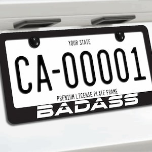 Pode incluir: Uma moldura de matrícula preta com a palavra BADASS em letras maiúsculas brancas em negrito na parte inferior. A moldura envolve uma matrícula branca com o texto YOUR STATE no topo e a sequência alfanumérica CA-00001 no centro.