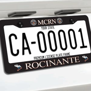May include: Black license plate frame with a white plate. The plate reads "CA-00001" in bold black font. The frame has the text "MCRN YOUR STATE" and "PREMIUM LICENSE PLATE FRAME ROCINANTE".