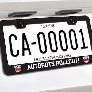 May include: Black license plate frame with the text "CA-00001" and "AUTOBOTS ROLLOUT!" The frame has a black border and the license plate is white. The license plate frame also has the text "YOUR STATE" and "PREMIUM LICENSE PLATE FRAME".