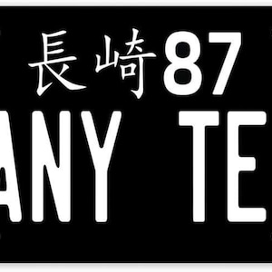 May include: Black license plate with white text that reads "ANY TEXT". The Japanese flag is in the upper left corner, with Japanese characters and the number 87. The plate has mounting holes.