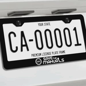Puede incluir: Un marco de matrícula negro con el texto blanco "PREMIUM LICENSE PLATE FRAME" y "SAVE THE MANUALS" junto a un icono de palanca de cambios. El marco está montado en un vehículo blanco, rodeando una matrícula blanca con "YOUR STATE" y "CA-00001".