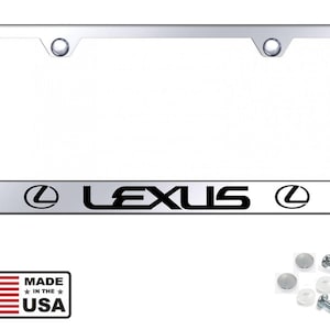 Könnte beinhalten: Ein verchromter Kennzeichenrahmen mit dem Wort "LEXUS" in schwarzer Schrift. Das Lexus-Logo erscheint auf jeder Seite des Textes. Enthält Befestigungsmaterial und einen "Made in the USA"-Aufkleber.