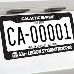 May include: A black license plate frame featuring the white text GALACTIC EMPIRE at the top and 501ST LEGION STORMTROOPER at the bottom, accompanied by a small white Stormtrooper helmet graphic on the left side of the bottom border.