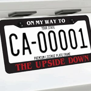 May include: Black license plate frame with the text "ON MY WAY TO YOUR STATE" at the top and "THE UPSIDE DOWN" at the bottom. The license plate reads "CA-00001".