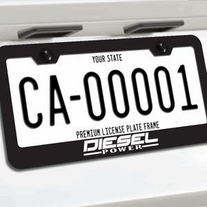 以下が含まれることがあります： 下部に白い文字でDIESEL POWERと書かれた黒いナンバープレートフレーム。フレームは、上部にYOUR STATE、中央にCA-00001と書かれた白いナンバープレートを囲んでおり、上部の両端にある2本の黒いネジで固定されています。